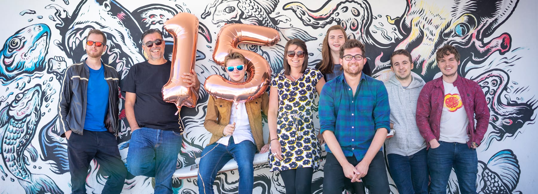 Digital Storm Team standing against a painted mural celebrating their anniversary with ballons